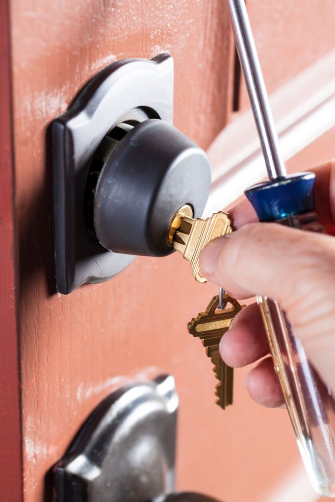 A locksmith inserting a golden key to a deadbolt lock on the front door