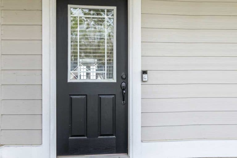 A black front door of a tan beige new construction house with siding, How Heavy Is A Fiberglass Door?