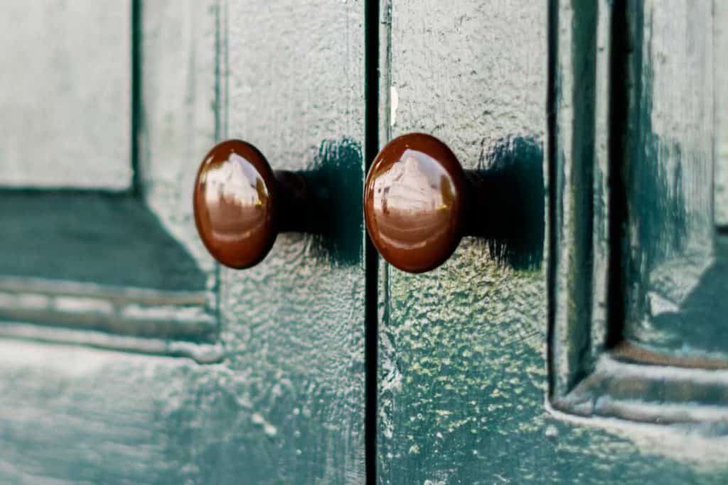 Close up of a green French door with dummy door knobs