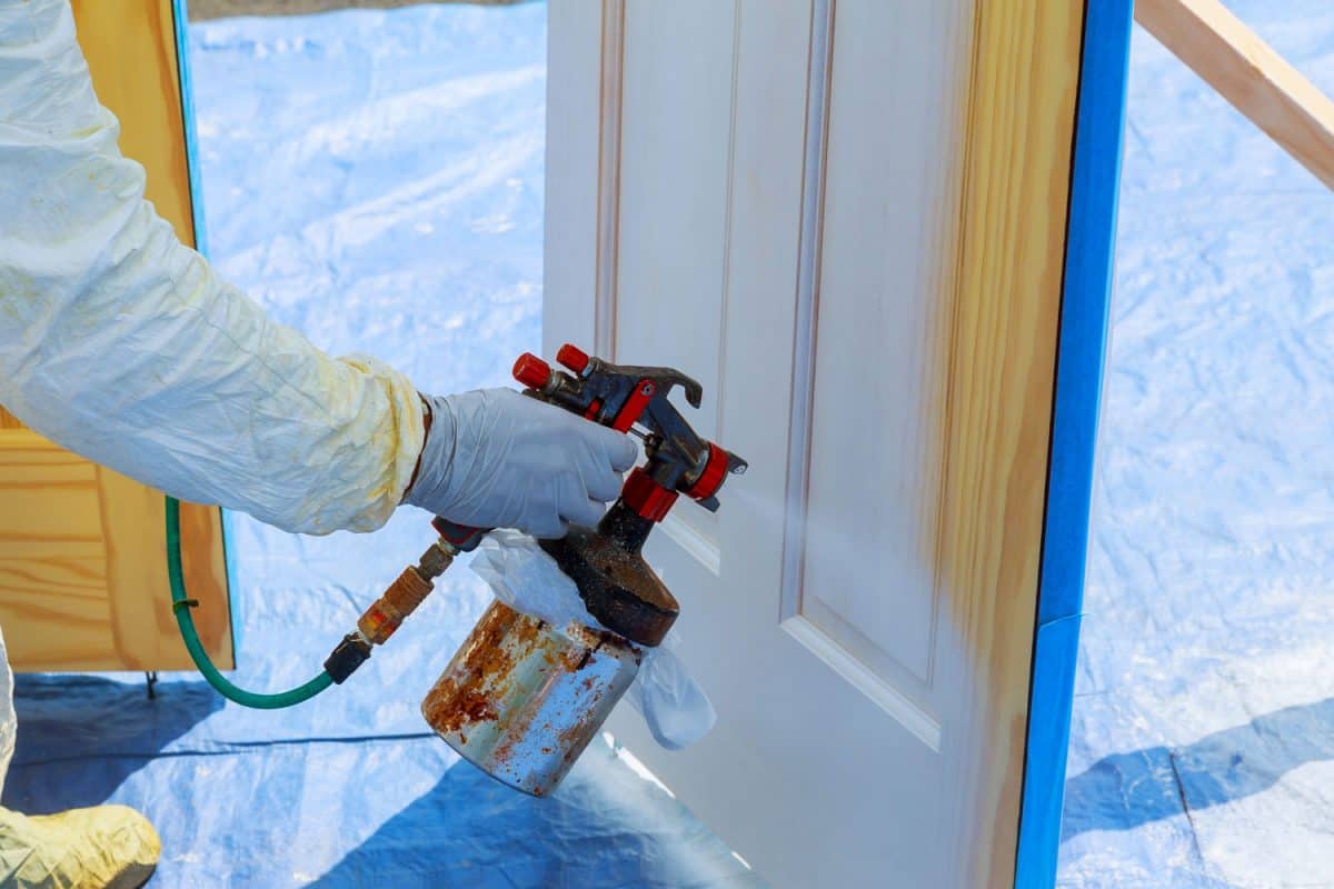 Worker with airbrush painting House repair paint the wooden door in white color with a spray