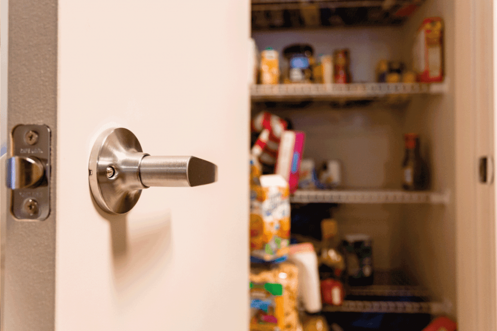A slightly out of focus kitchen pantry is shown that is half way empty. Focus on the pantry door handle. How To Childproof A Pantry Door