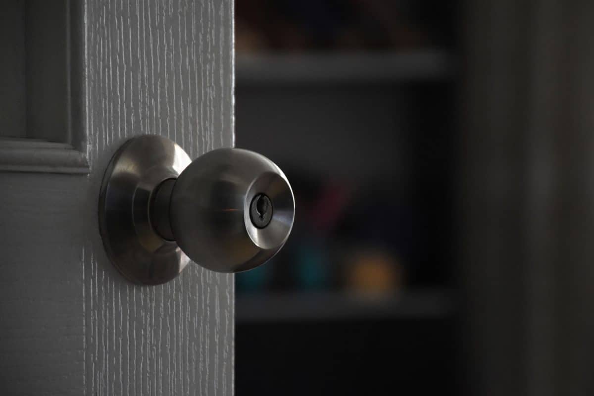 White wooden interior door, metallic circle doorknob and lock with the defocused living room, How To Fix A Passage Door Knob