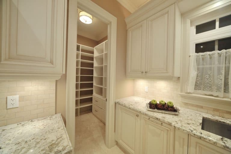 A gorgeous kitchen with an empty pantry and a marble countertop and cream cabinetry, How Wide Should A Pantry Door Be?