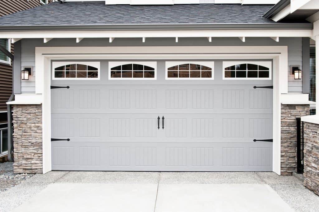 A gray single car garage door with decorative tiles on the walls and gray asphalt roofing