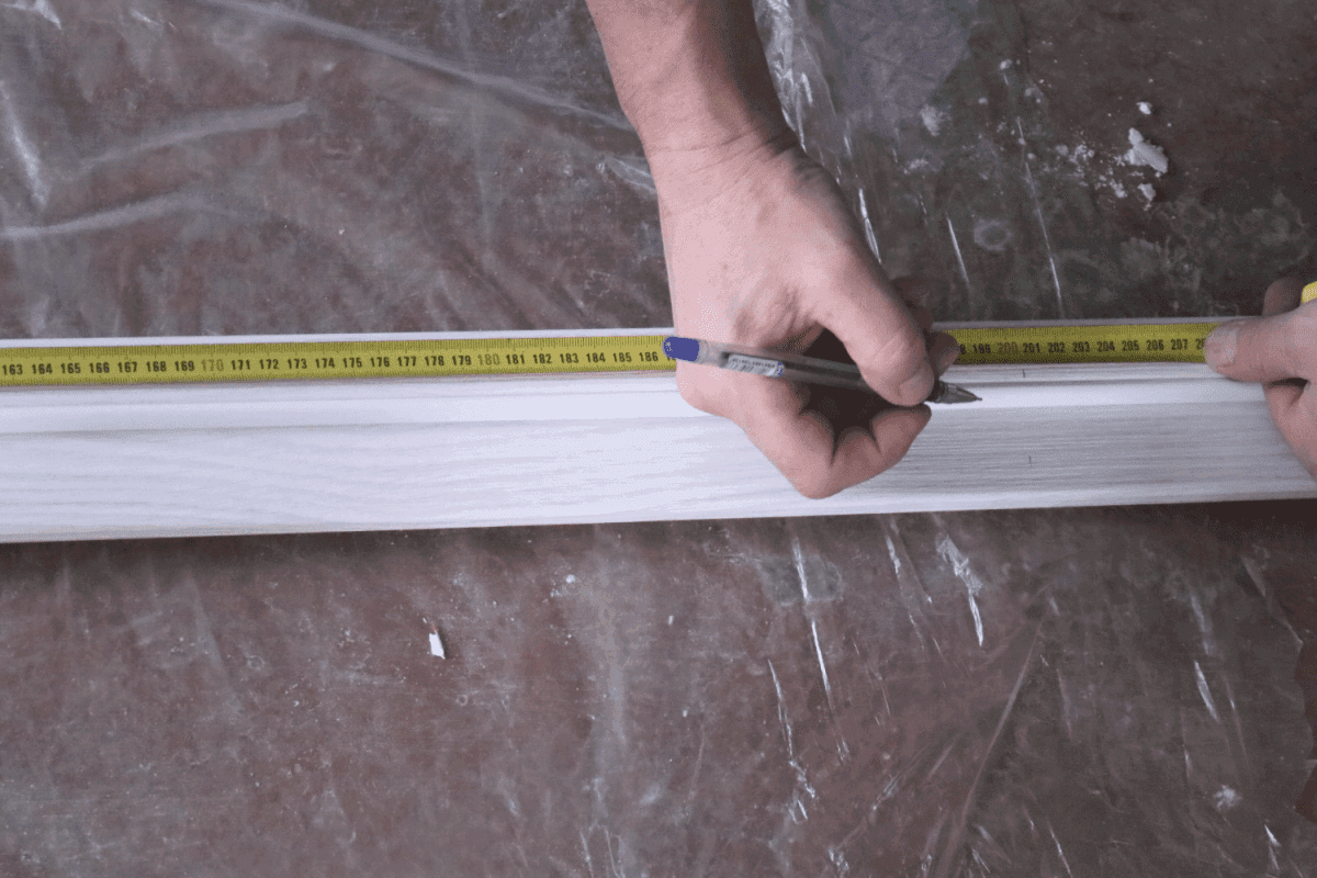 Measuring the length of the door casing made of light wood using a tape measure in the hands of the installer, marking the board with a pen