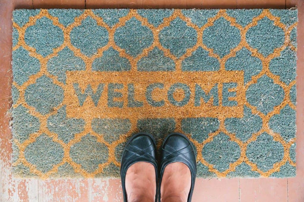Woman stands on a welcome mat on the porch of a home