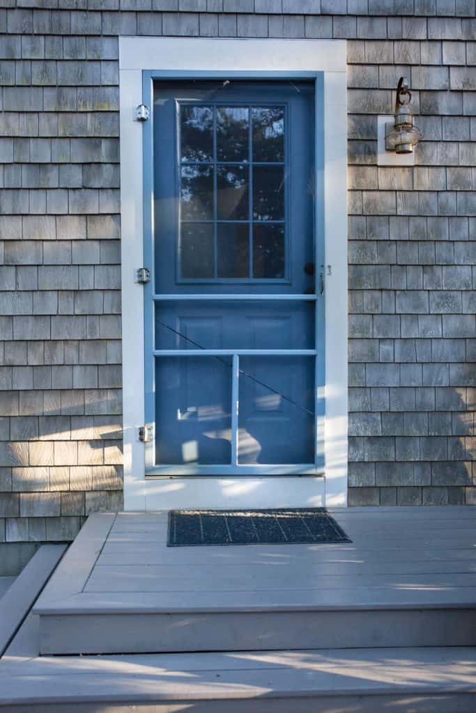 A blue screen door in front of a small country home