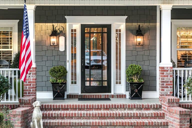 A classic themed front porch with brick stairs and an American flag raised in front, How Long Does It Take To Install A Storm Door