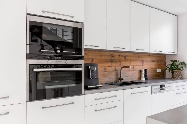A modern contemporary kitchen with white cupboards and white cabinetries with an oven and microwave on the side, How To Clean A KitchenAid Oven's Glass Door
