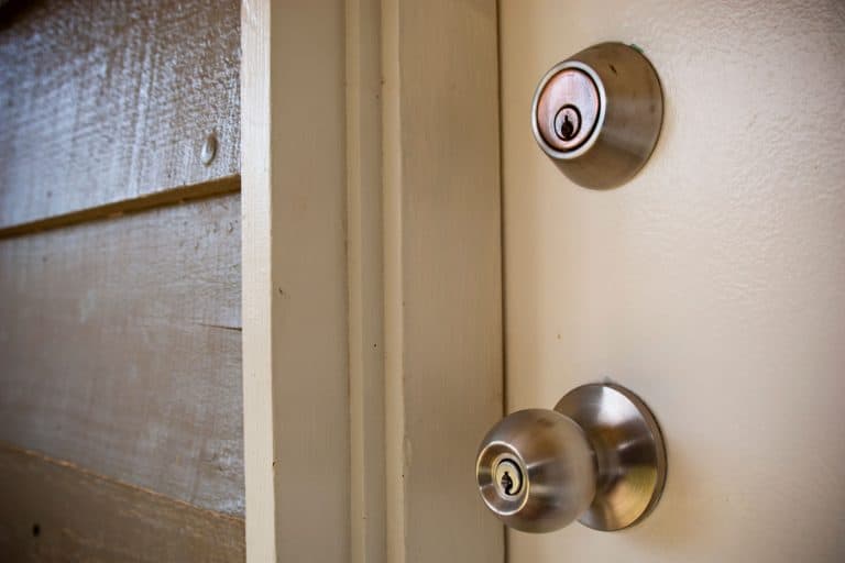 A white wooden front door with a stainless steel door with a deadbolt lock, How High Should A Deadbolt Be On A Door?