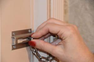 A woman locking the chain lock of her front door, How To Put A Chain Lock On A Metal Door