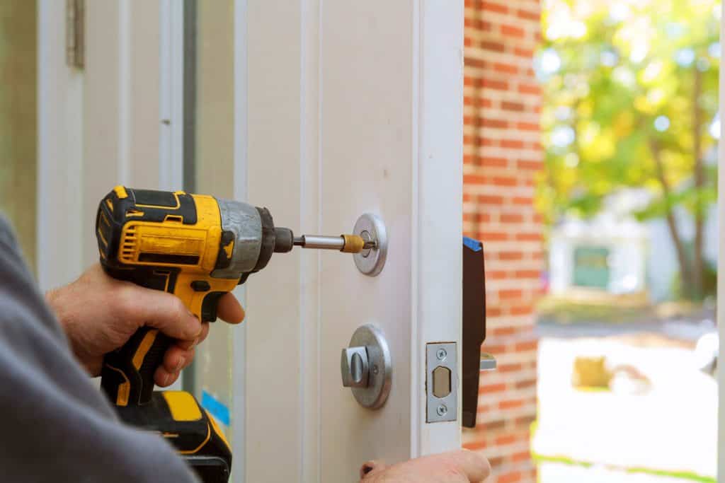 A worker installing a deadbolt lock into the front door of a house