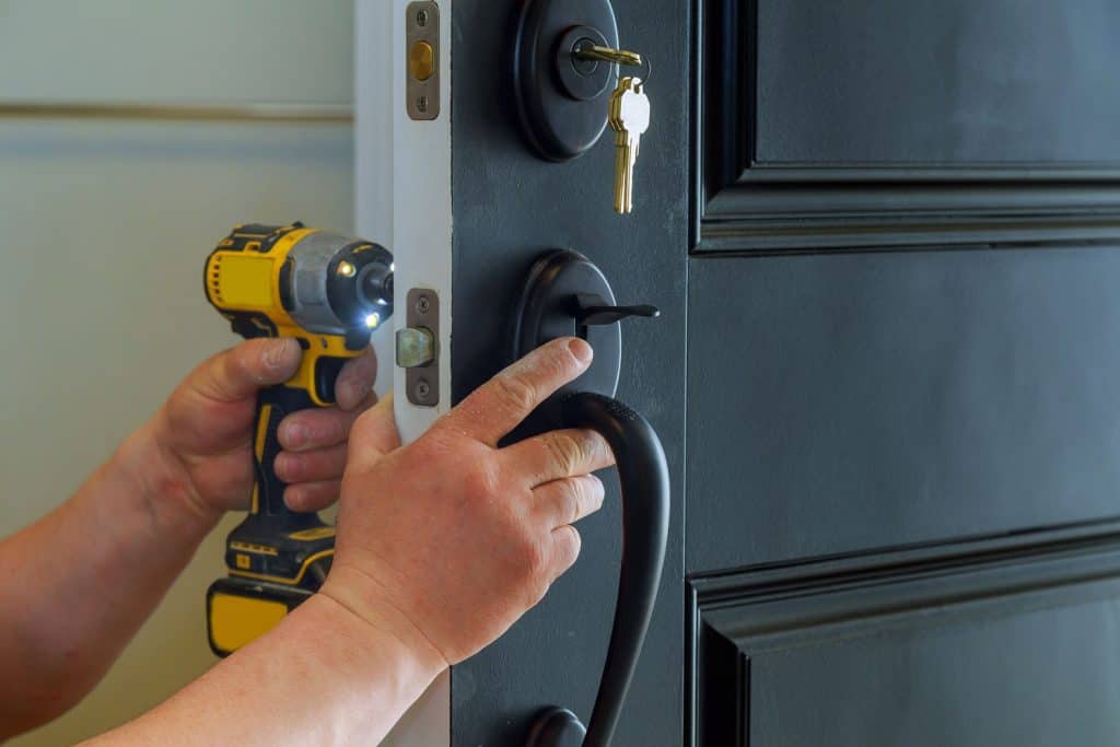 A worker using a portable drill in installing the deadbolt lock
