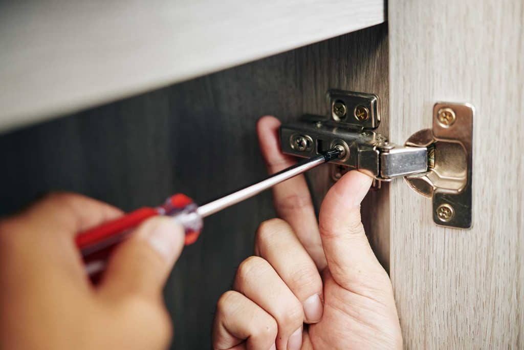 Handyman assembling kitchen cabinet and screwing door hinge