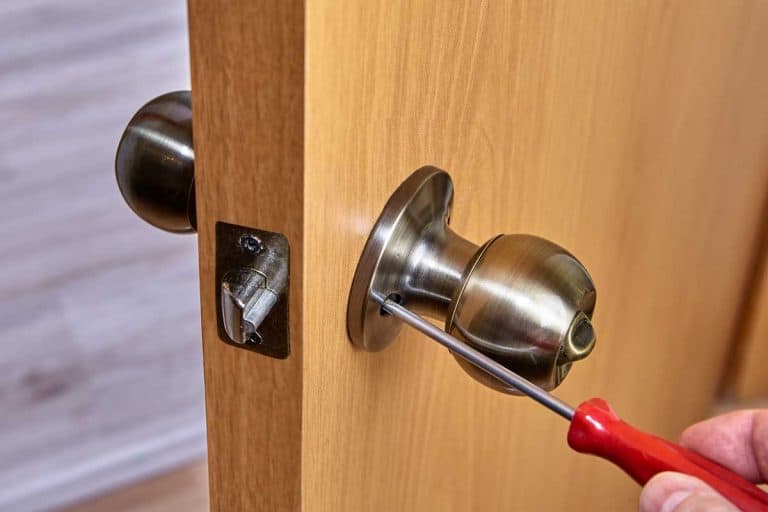 Adjusting screw of a bronze-colored spherical door handle in an interior door, How To Fix Loose Door Handle Or Door Knob Screws