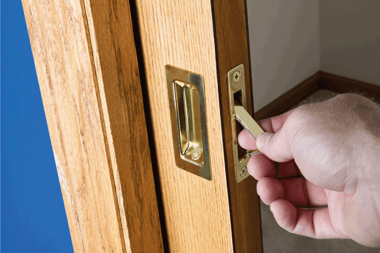Male hand reaching for the edge pull on the handle of a concealed wooden pocket door which has been slid back into the wall cavity. Should Pocket Doors Be Solid Or Hollow