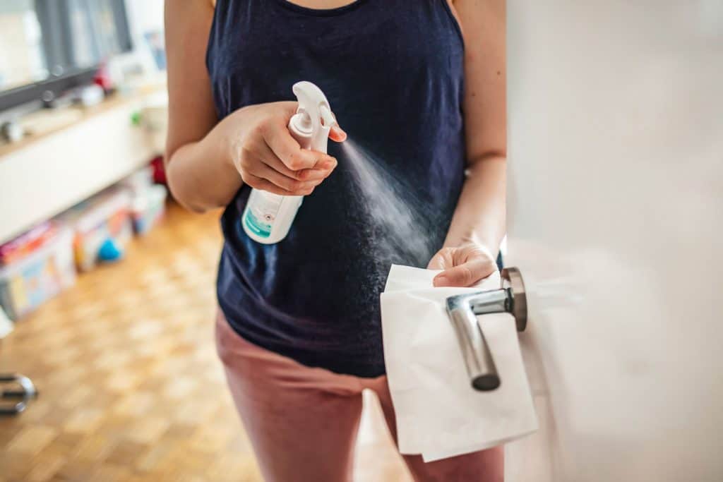 Woman cleaning a door handle with a disinfection spray and disposable wipe