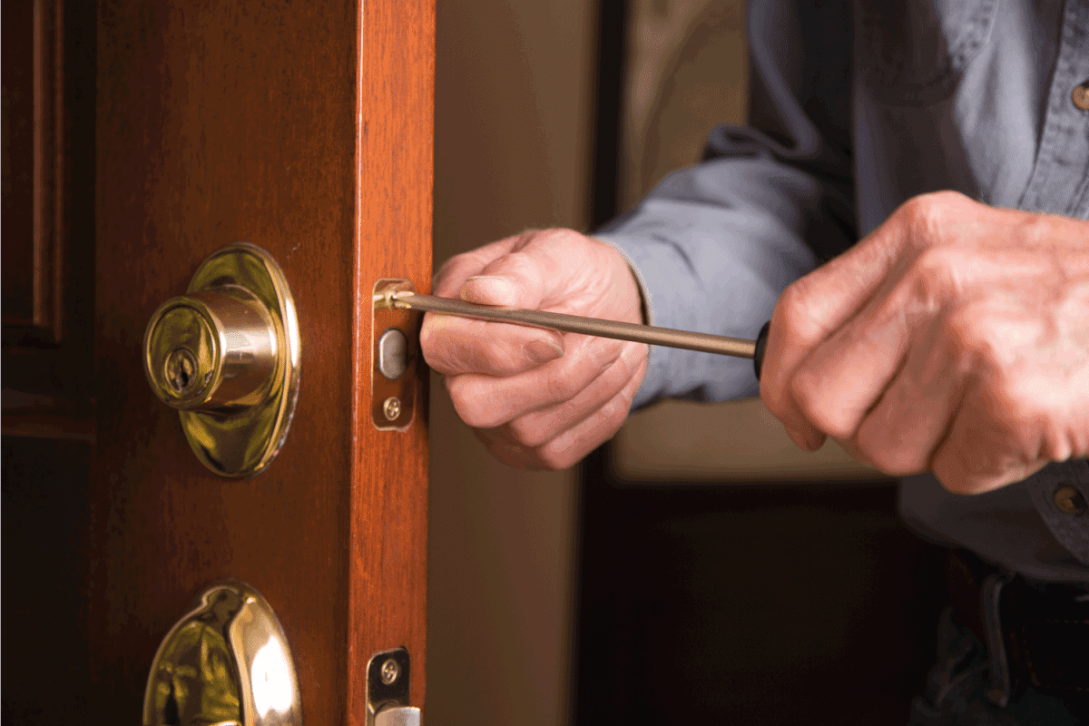 Worker in blue uniform or homeowner installing or repairing door knob on an exterior door