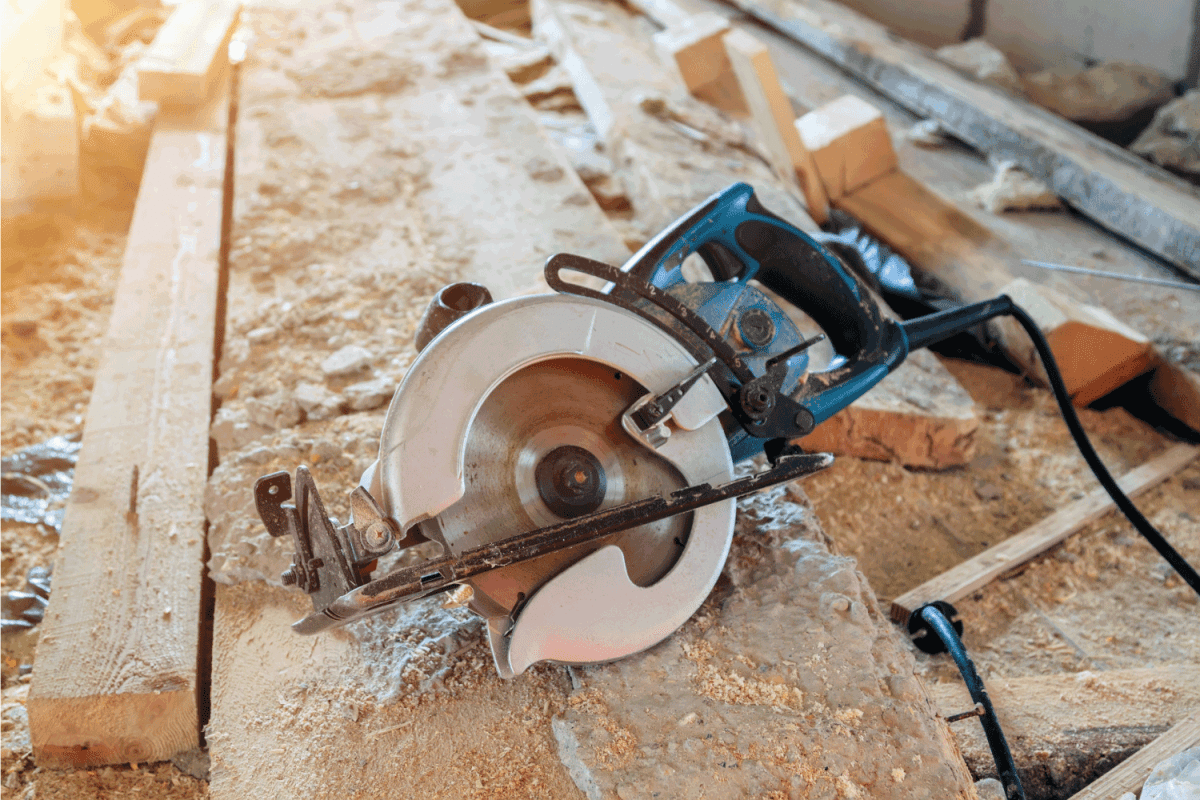 electric portable circular saw is on wooden board in house under construction