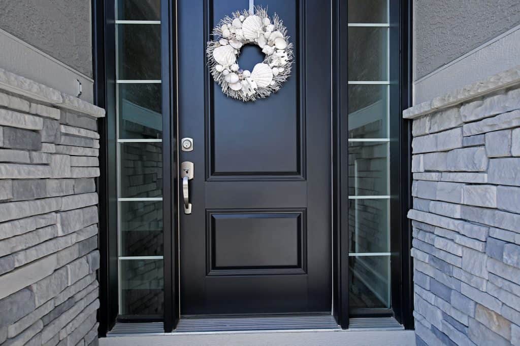 A black door with silver hardware, glass panes and a wreath hanged on the front door