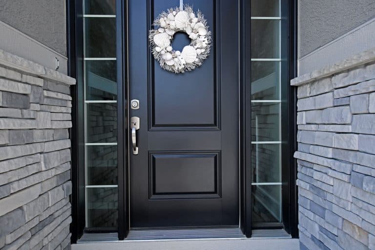 A black door with silver hardware, glass panes and a wreath hanged on the front door, What Color Hardware Goes With Black Doors?