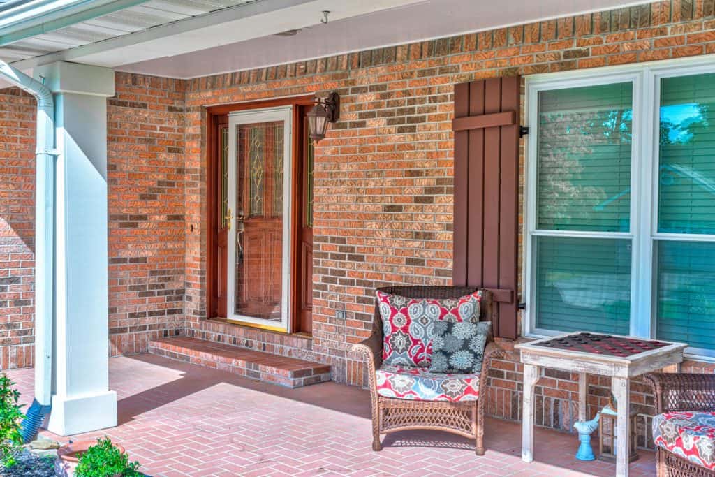 A brick walled front porch with a wooden front door and a storm door