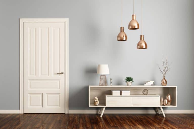 A minimalist themed living room with a white door, wooden flooring and a small cabinet with brass pot and figurines, Should Door Frames Be The Same Color As The Door?