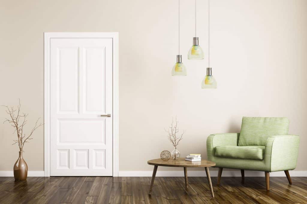 A white door inside a minimalist themed living room with dangling lamps and a green accent chair