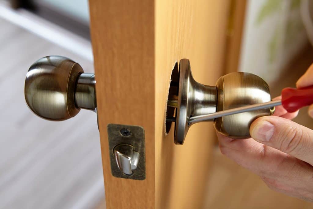 Carpenter fixes door knob with lock and latch on new door.

