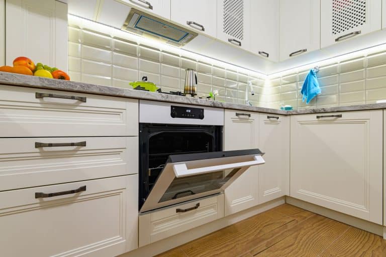 Small white cozy and comfy contemporary classic kitchen interior, electric oven door is open, Does An Oven Door Have A Cleaning Slot? [How To Access It]