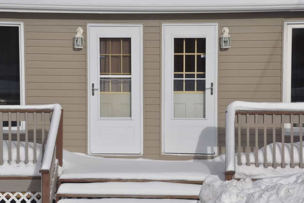 Two white storm doors in a front porch filled with snow
