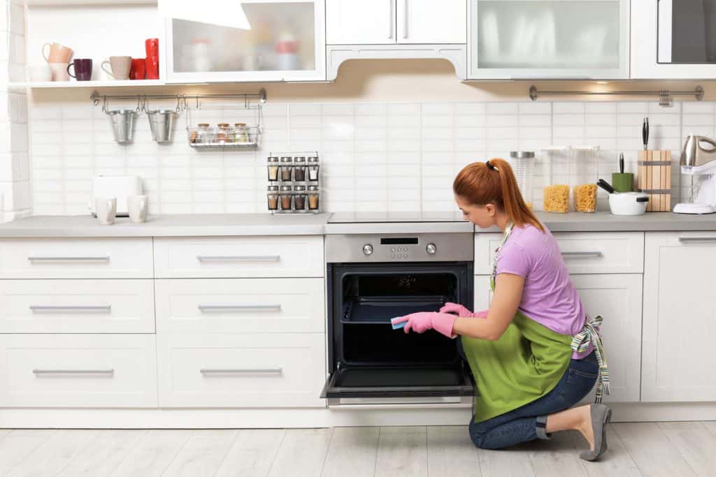Woman cleaning oven tray with rag in kitchen
