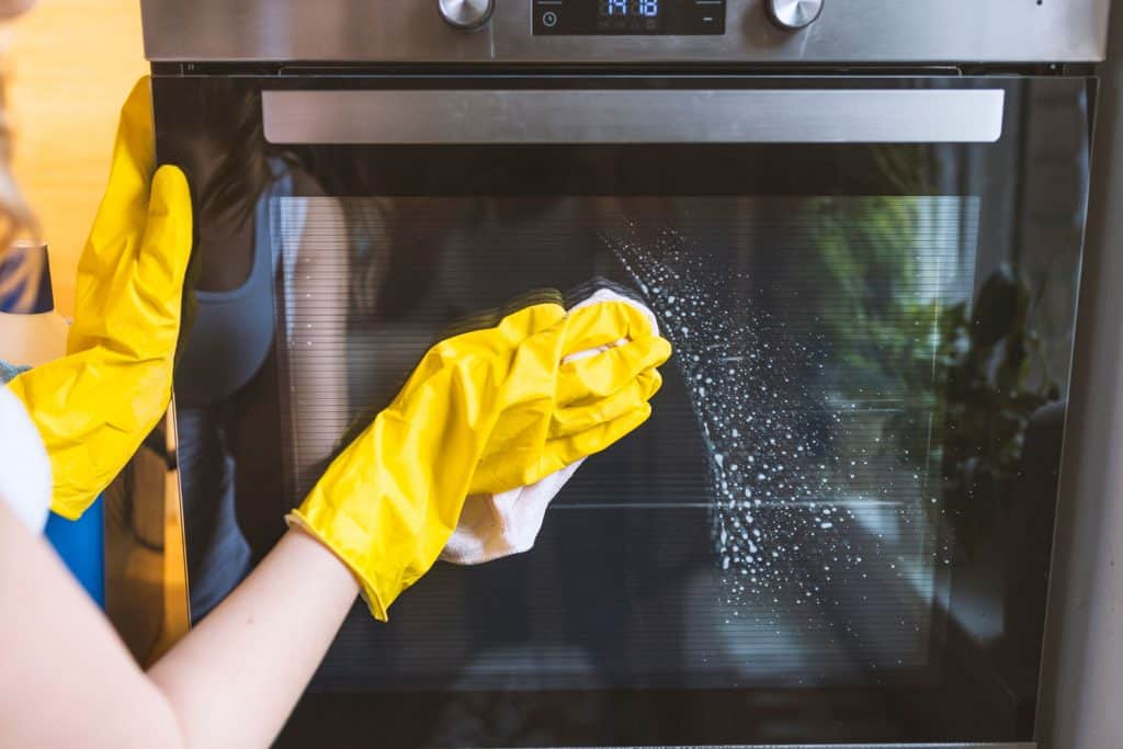 female hand with yellow protective gloves cleaning oven door