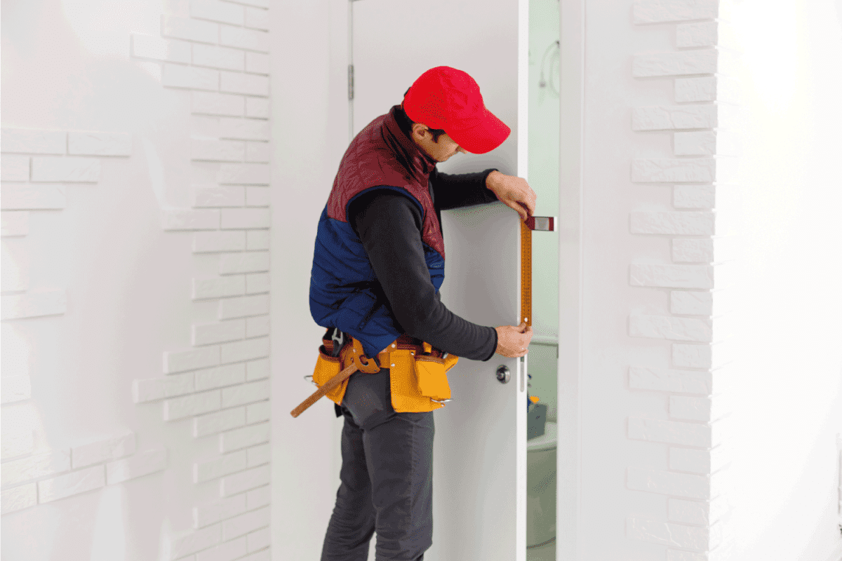 young man measuring an installed door in a new house construction site