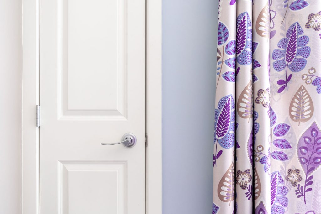 Home interior showing colonial closet door with purple curtain decor and light blue painted wall