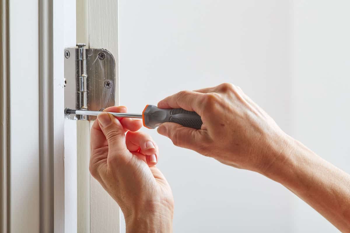 Hands with screwdriver fixing a door hinge