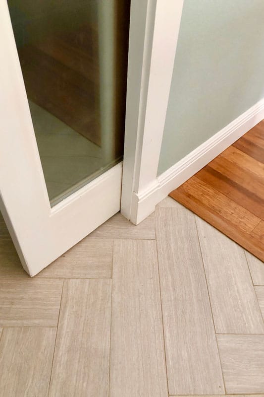 Low angle closeup of white pocket door and frame with parquet tile floor