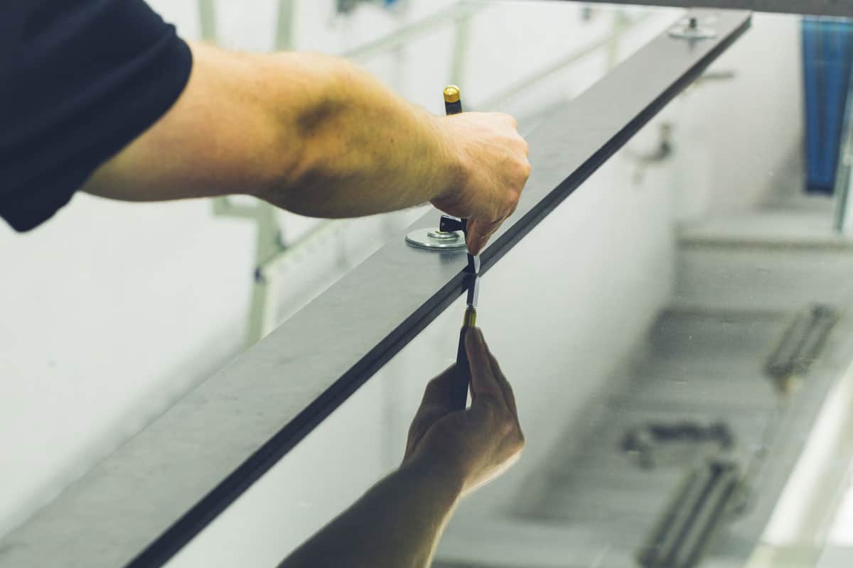 An employee in a glass factory cuts a large sheet of glass with the help of specialized tools